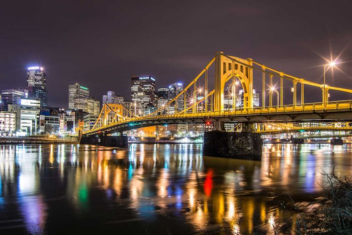 A yellow bridge illuminated at night in Pittsburgh.
