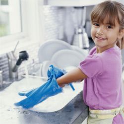 A young girl washing dishes while wearing gloves.