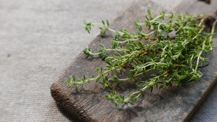 Fresh thyme resting on a rustic wooden chopping board.