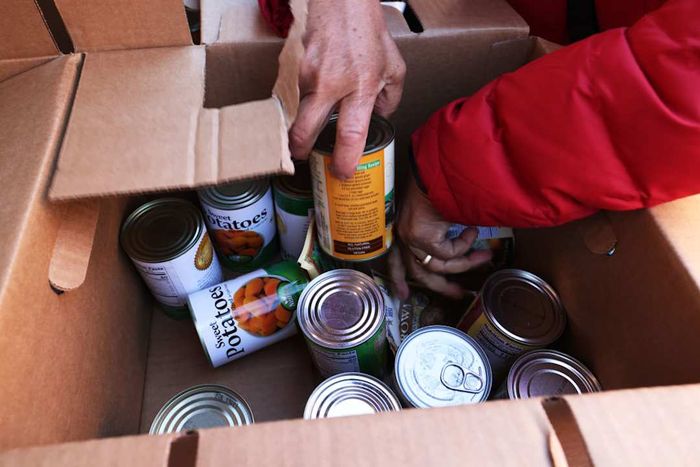 Individuals selecting canned goods from a packed box.
