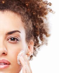 A young woman applying moisturizer to her face.