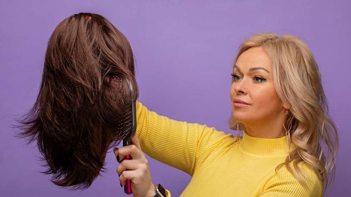 A woman holding a wig is shown