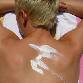 A young man applying sunscreen on his back.