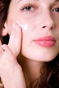 A woman gently applying moisturizer to her face.