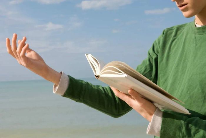 Image of a young man engrossed in reading a poetry book by the beach