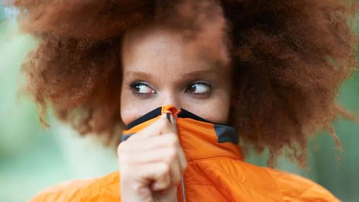 A woman in an orange sweater pulling it over her mouth