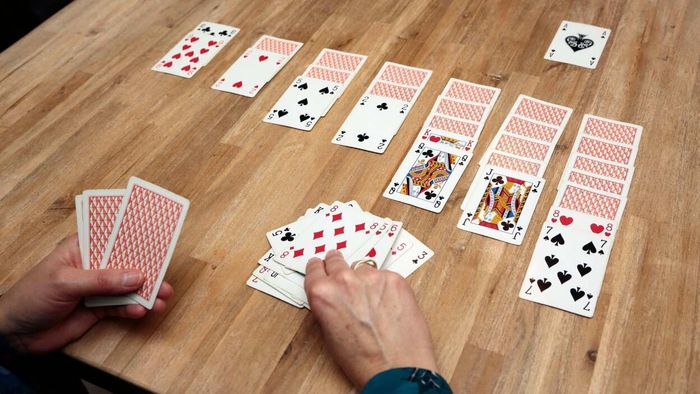 A person playing a solitaire card game on a wooden table