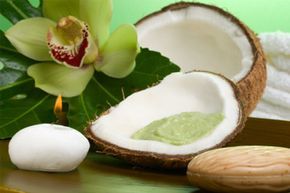 Avocado coconut scrub in a coconut shell, orchid flower (Cymbidium sp.), tropical plants, soap, and aromatic candles.