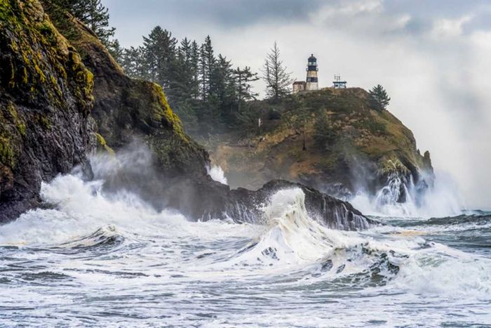 Waves crashing against the coast in the Pacific Northwest with a lighthouse perched on a cliff.