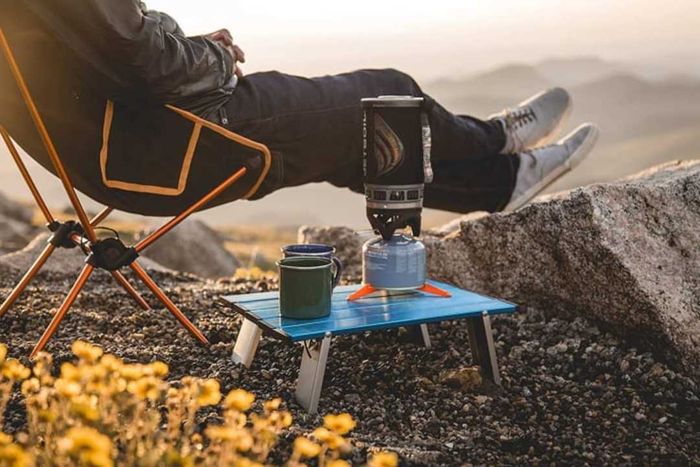 A person using a Trekology Personal Beach Table outdoors with a mug