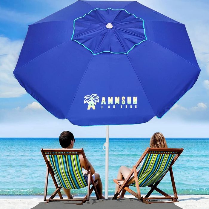 Two individuals relaxing on a beach under an AMMSUN Heavy Duty High Wind Beach Umbrella