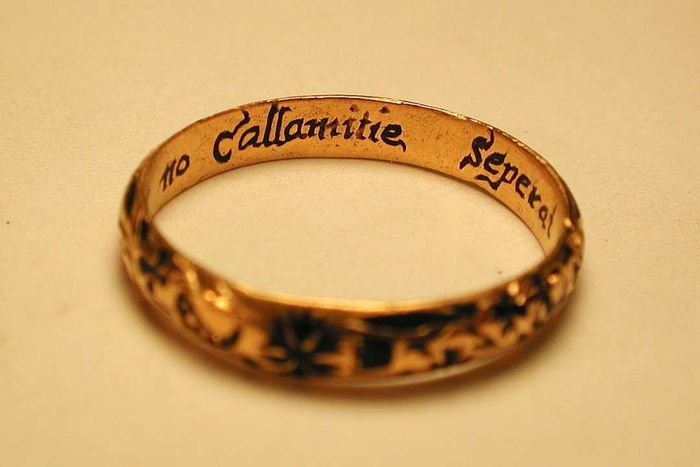 A gold posy ring featuring intricate decoration on the outer surface. The engraving reads ‘Let no callamitie seperat amitie.’ which translates to ‘Let no calamity separate friendship.’