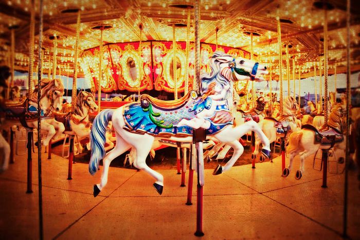 A vibrant Merry Go Round captured in close-up, highlighting a beautifully decorated white horse adorned with intricate blue and green patterns.