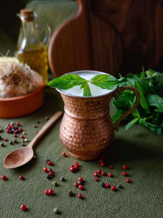 Freshly made buttermilk garnished with mint leaves, served in a copper mug on a khaki-green tablecloth.