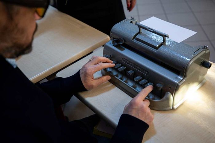 A man is typing a braille letter using a Perkins Brailler.
