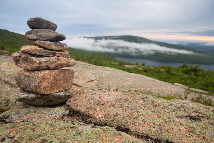 A cairn on rocks with low clouds over a lake in Acadia National Park, Maine