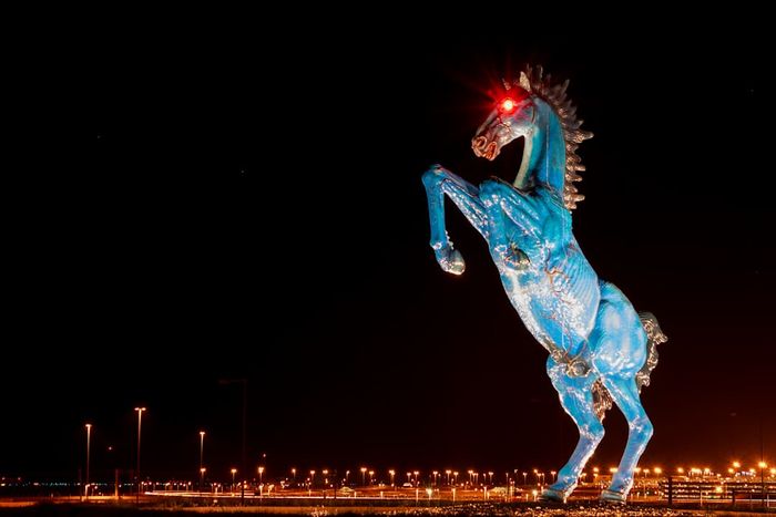 A Mustang statue illuminated at night, its red eyes glowing