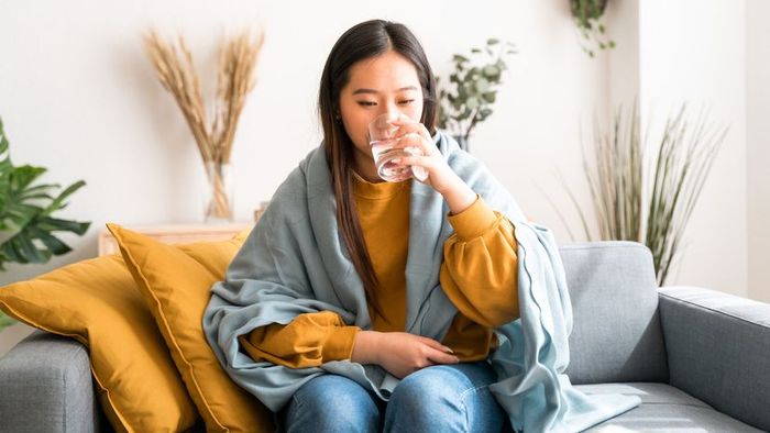 A woman of Asian descent at home, drinking water while taking medication.