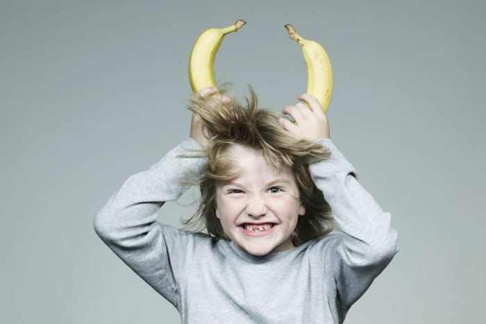 A boy holding bananas to his head, mimicking devil horns.