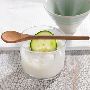 A bowl filled with yogurt and cucumber slices.