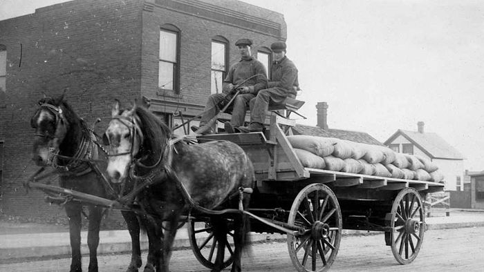 Two delivery men sit atop a horse-drawn wagon, ca. 1900