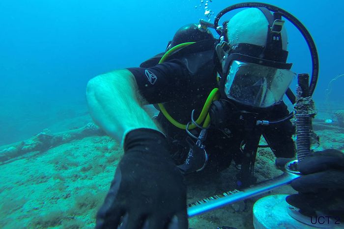 A scuba diver repairs an undersea steel cable.