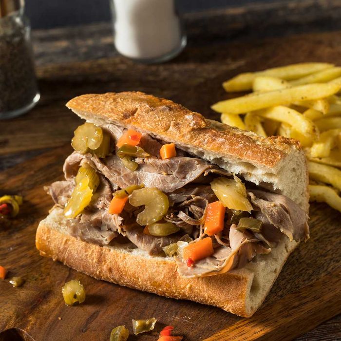 An Italian beef sandwich displayed on a wooden cutting board.