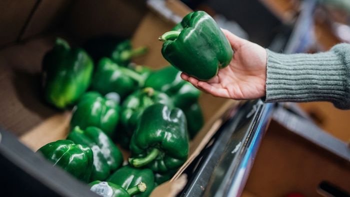 A female hand holding a green pepper in a supermarket.