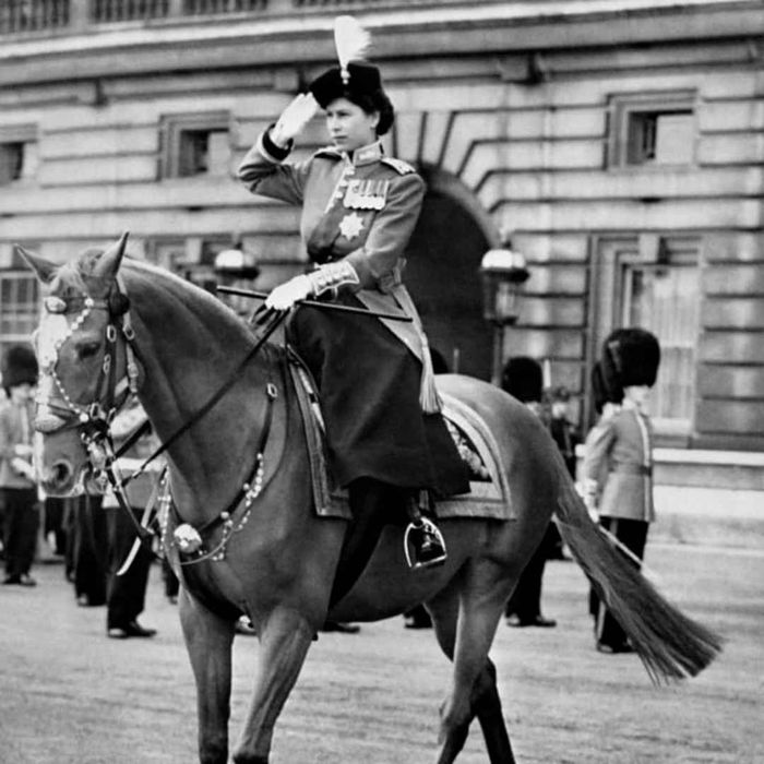 Queen Elizabeth II of Britain riding side-saddle on a horse and offering a salute.
