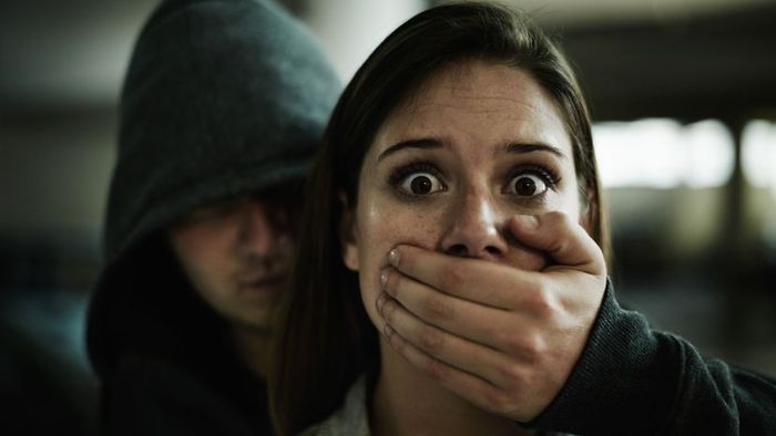 A man covering the mouth of a frightened woman.
