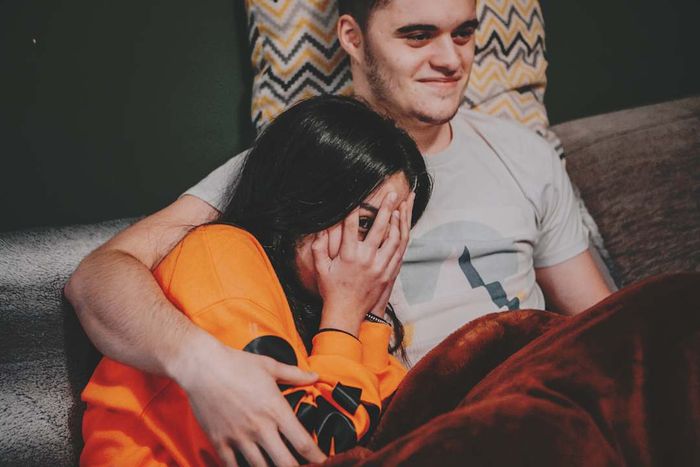 Young couple watching a scary show; woman is covering her face with her hands