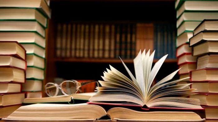 A collection of books surrounding an open book and a pair of glasses.