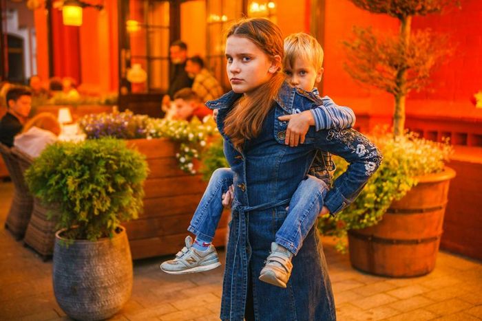 An older sister carrying her younger brother on her back in a bustling market