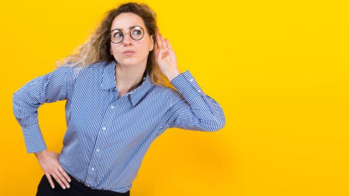 A woman cupping her ear to enhance her listening experience.