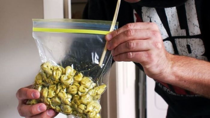 A man using a straw to remove air from a bag filled with pasta.