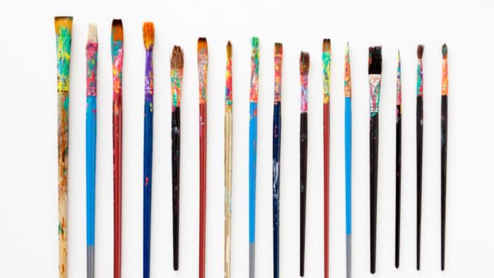A collection of used paint brushes against a white backdrop.