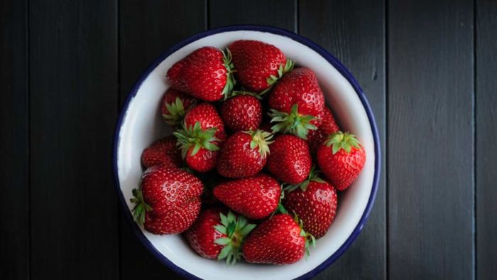 A wooden table holding a bowl filled with strawberries.