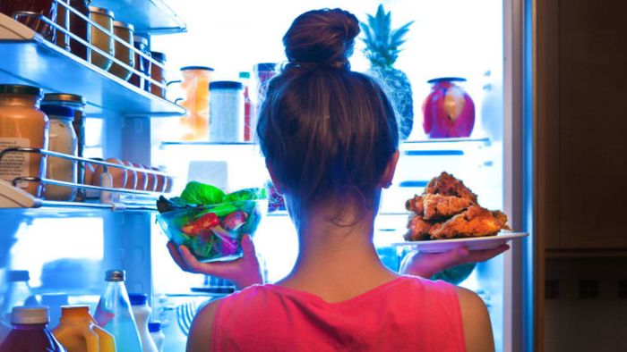 A woman retrieving food from a refrigerator.