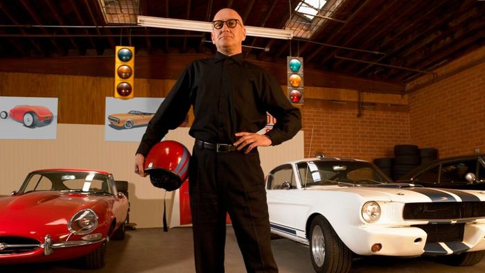 A man posing next to two iconic vintage cars.