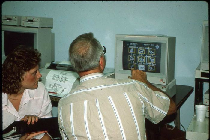 Two individuals standing in front of a vintage computer