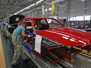 At a BMW manufacturing facility, employees are seen assembling a red car on the production line.