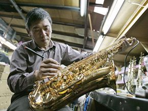 An Asian man constructing a saxophone in a manufacturing facility.