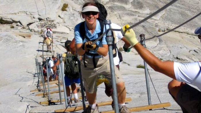 Adventurers scale Half Dome, the iconic granite formation in Yosemite Valley, by navigating a steep cable ladder.