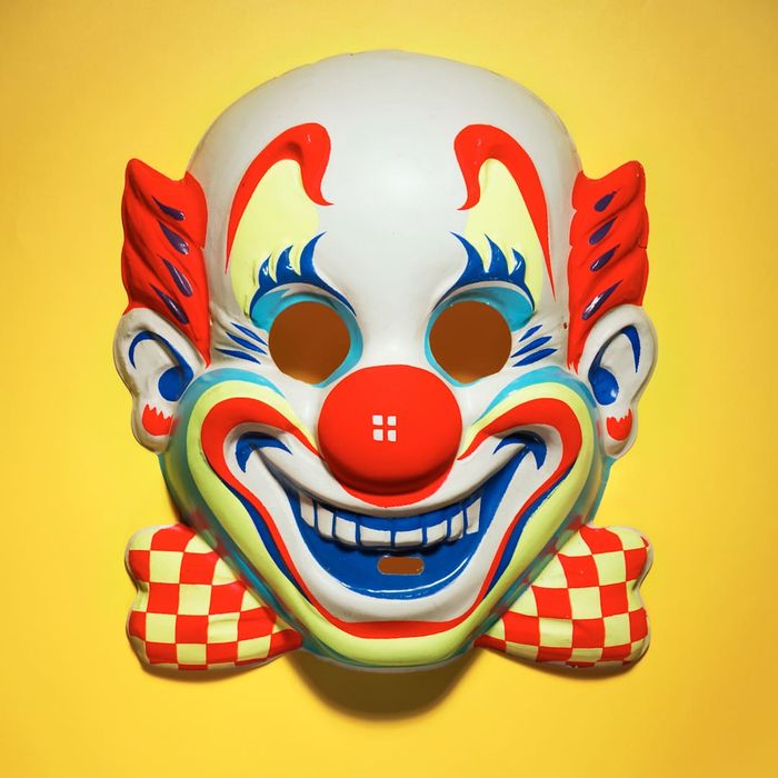 A clown mask set against a bright yellow background