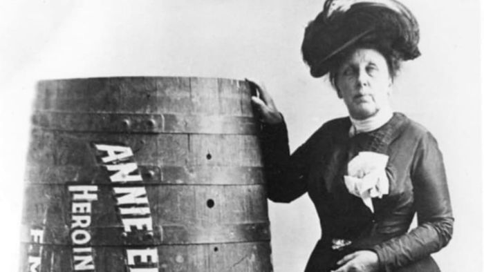Annie Edson Taylor, the first person to survive a barrel ride over Niagara Falls, proudly stands beside her unconventional vessel.