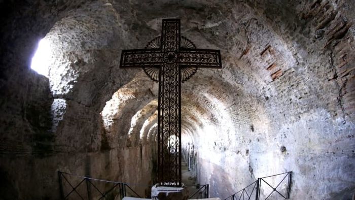 A cross is prominently displayed within the Roman catacombs