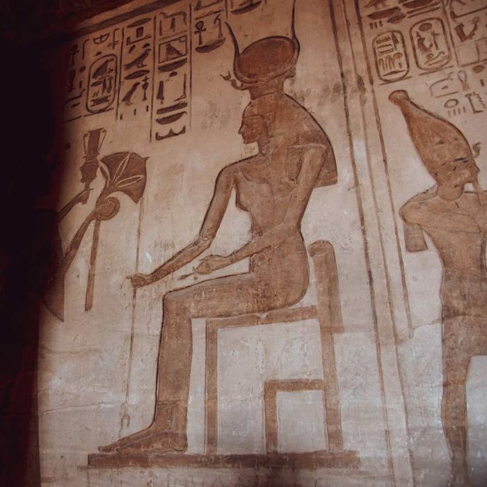 Egyptian wall art depicting a seated woman with tall, slender horns supporting a sun disk.