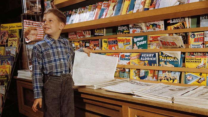 A child is shown standing beside a stack of comic books.