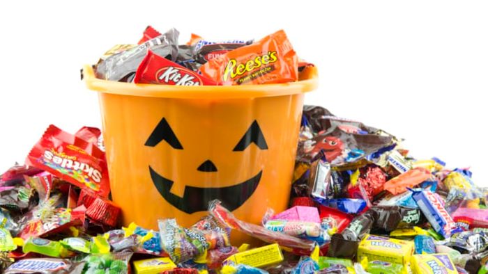 An orange bucket filled with Halloween candy, surrounded by more candy.