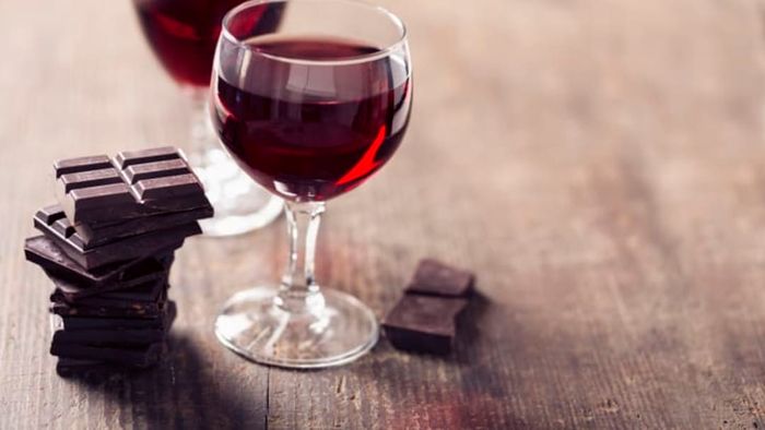 Two glasses of red wine placed on a table alongside chocolate treats.